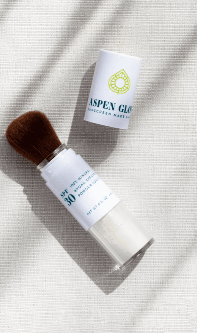 Aspen Glow SPF 30 sunscreen container beside a makeup brush.