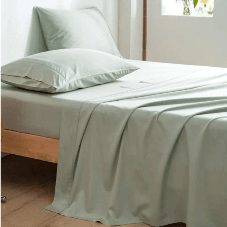Made bed with light green sheets and pillows in a minimalist room.