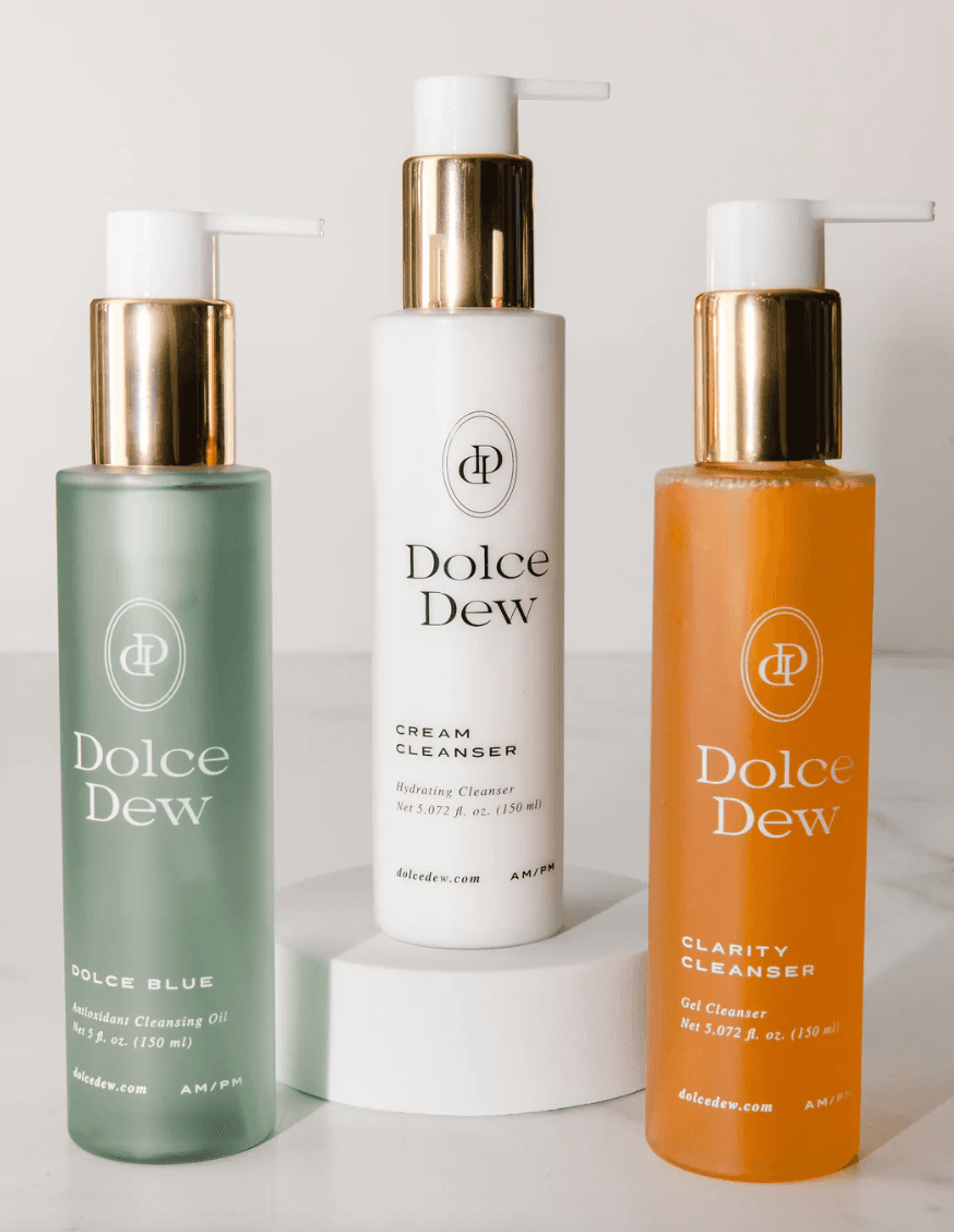 Three Dolce Dew skincare bottles arranged on a white surface.